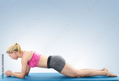 Young woman doing full body yoga exercise on blue mat