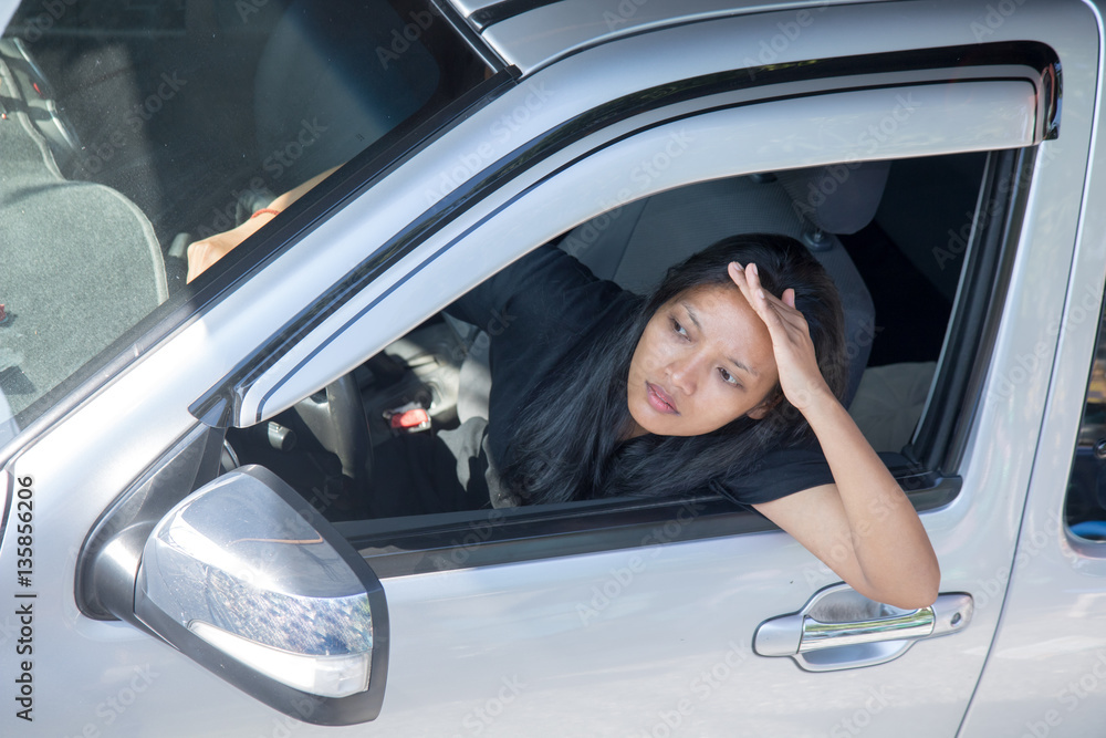 Woman sticking out of the open car window and with shading hand looks into the distance.