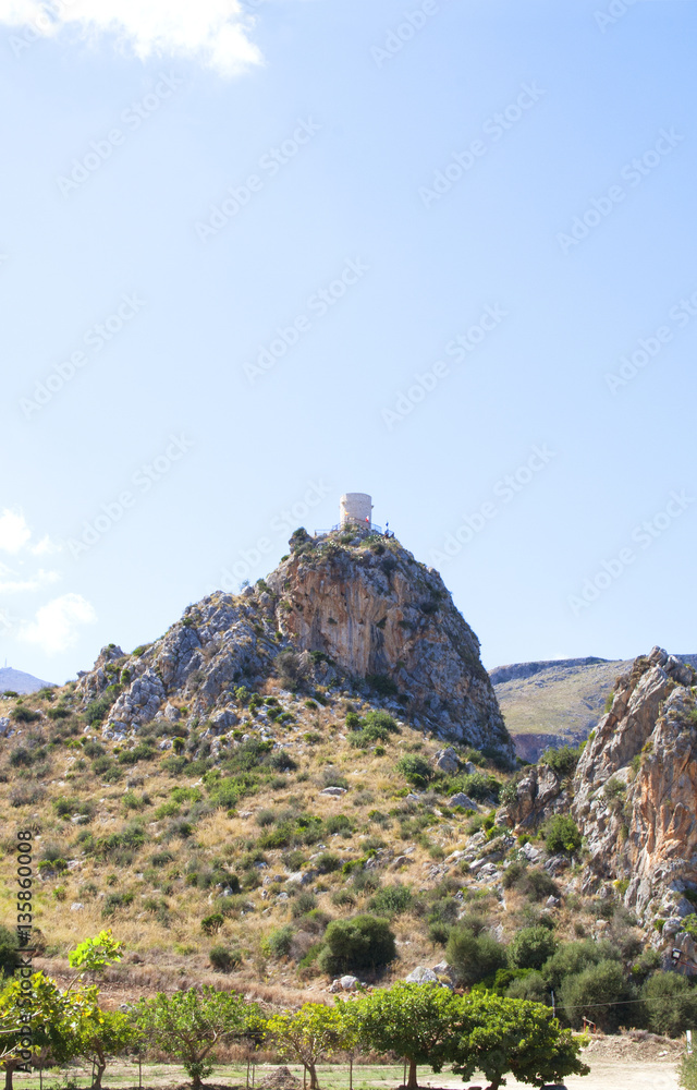 An ancient tower in the mountains can be seen from the town of Scopello as well as the tipical grape trees An ancient tower in the mountains can be seen from the town of Scopello as well as the tipical grape trees