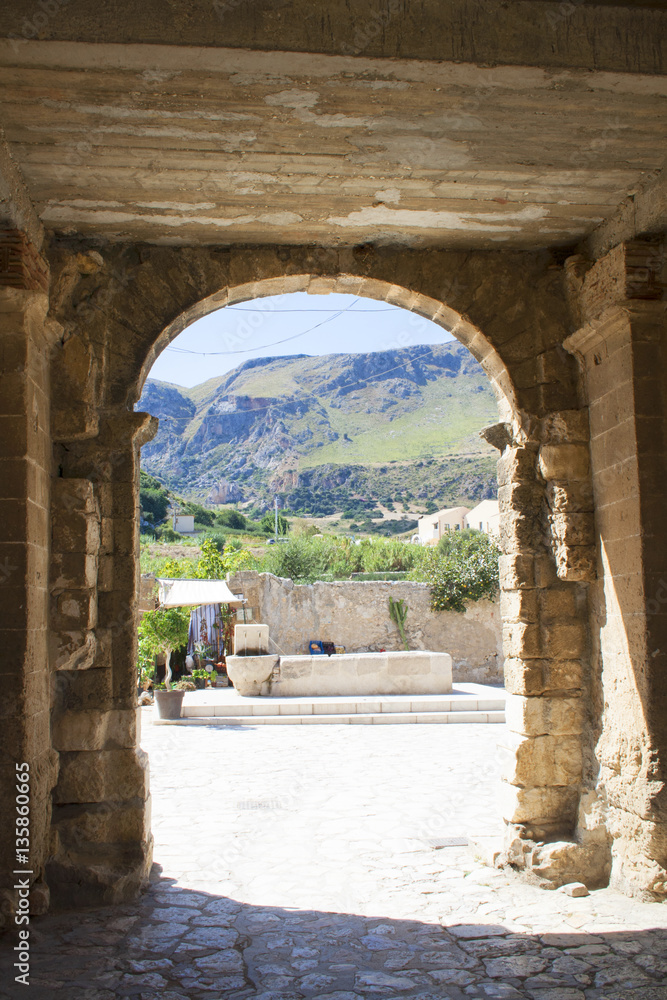From inside the entrance of Scopello Village you can see the public water cistern and the mountains as backdrop