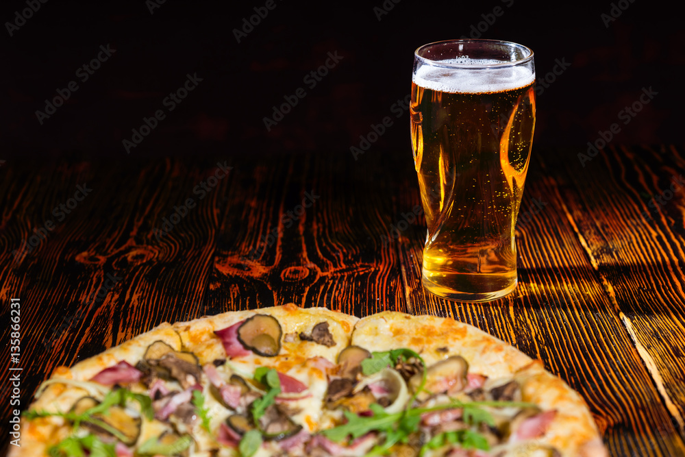Pizza with ham on wooden table near a glass of beer