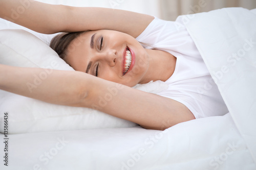 Woman stretching in bed after wake up, entering a day happy and relaxed after good night sleep. Sweet dreams, good morning, new day, weekend, holidays concept