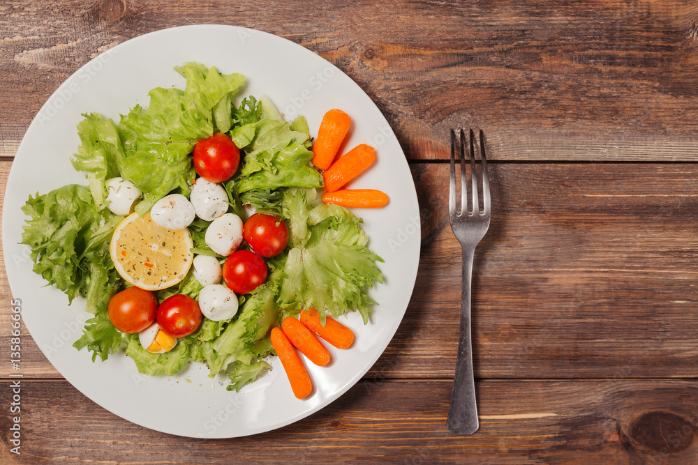 Tasty salad with cherry tomatoes, salad leaves, lemon, spices, carrot and quail eggs on wooden table with fork. Top view Tasty salad with cherry tomatoes, salad leaves, lemon, spices, carrot and quail eggs on wooden table with fork. Top view