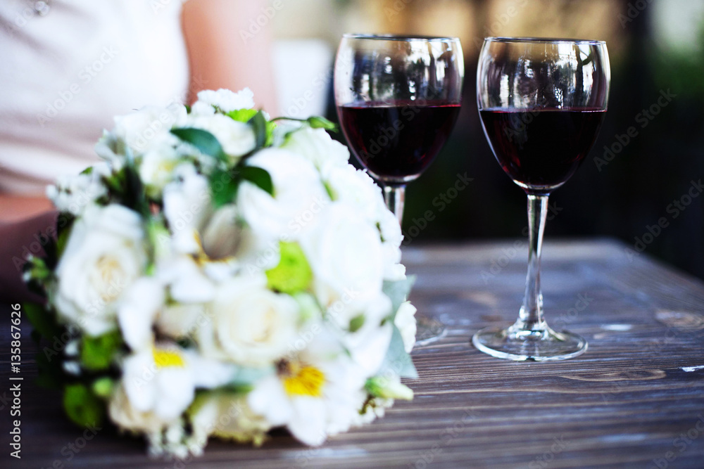 A bouquet of flowers and two glasses of wine on a wooden table. A bouquet of flowers and two glasses of wine on a wooden table.