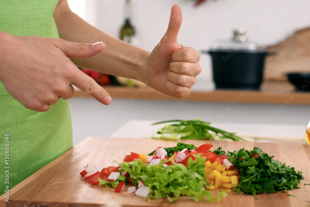 Close up of  woman's hands cooking in the kitchen. Housewife offering ​​fresh salad with thumbs up. Vegetarian and healthily cooking concept