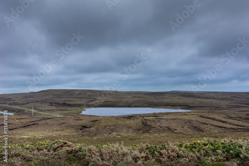 North Coast, Scotland - June 6, 2012: Lake in relative flat waste land behind Dunnet Head lighthouse. Cloudy gray-blue sky. Terrain is rather brown than green. 