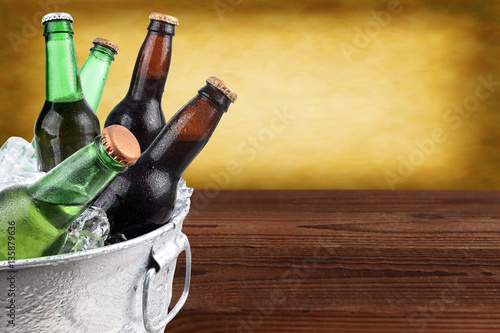 Closeup of a metal ice bucket filled with assorted beer bottles. Horizontal format with copy space and warm background.