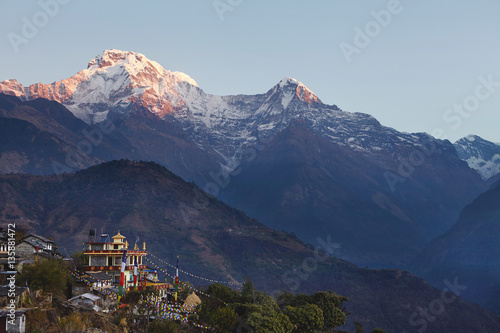 Rural life in front of gigantic Himalayas  Nepal. Incredible view of Nepali village with Buddhist flags strung along  spectacular ancient mountains with white craggy peaks standing high in background