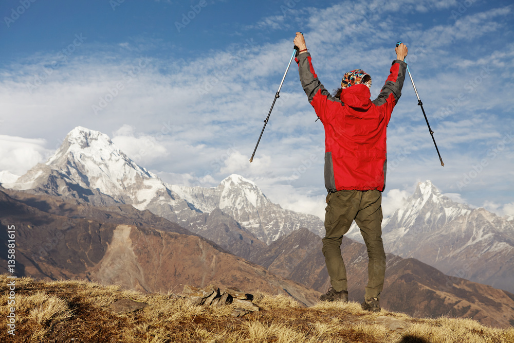 Elated and blissful young hiker cheering with his arms raised in the sky after trekking in highlands. Face to face with the majestic and grand Himalayan mountains with snowy summits and passes