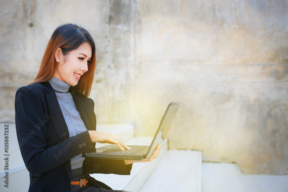 The business women : young women people business woman sit down, The beautiful business women hold laptop and smiling , space brown wall background for texture. The business women : young women people business woman sit down, The beautiful business women hold laptop and smiling , space brown wall background for texture.