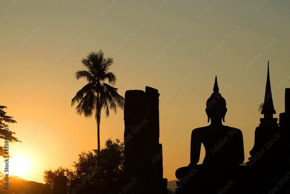 Silhouette of the ancient sculptures of the seated Buddha at sunset. Park of Sukhothai, Thailand