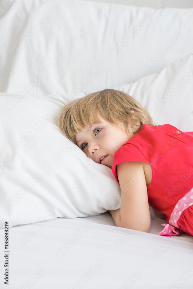 Little girl lies in red dress on white bed Little girl lies in red dress on white bed