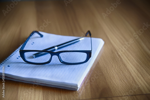 Glasses and pen lie on a clean notebook on a wooden table