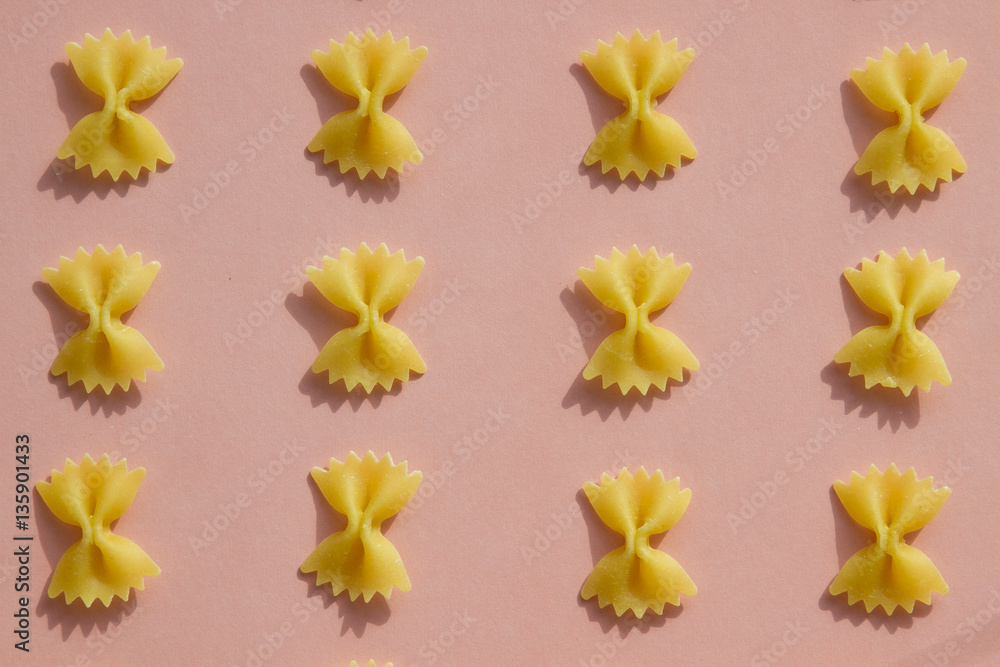 Maсaroni or pasta bow shape in row on pink background Maсaroni or pasta bow shape in row on pink background