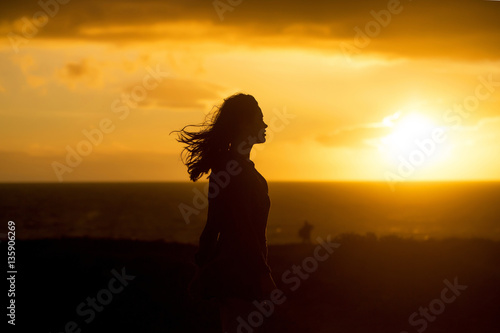 Black silhouette of pretty girl on sea beach at sunset