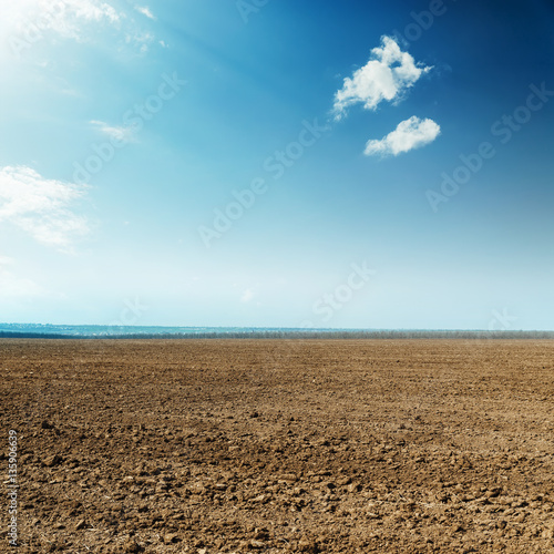 black plowed field and clouds in blue sky