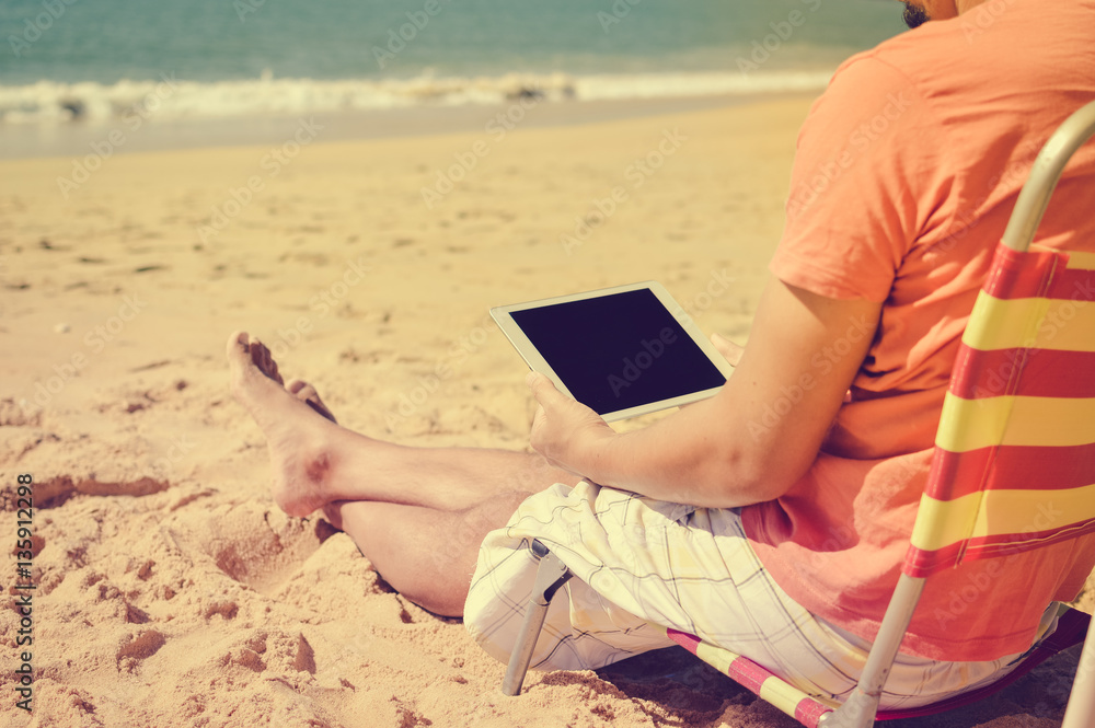 Business man relaxing working using tablet computer on the sunny beach outdoors background. Businessman working enjoying remote location
