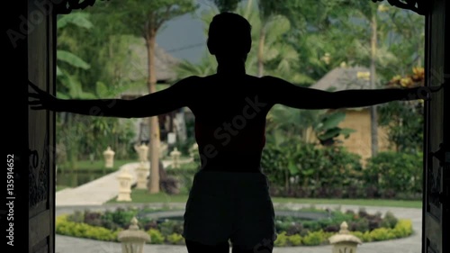 Young woman opening door and walking out on porch in country house
