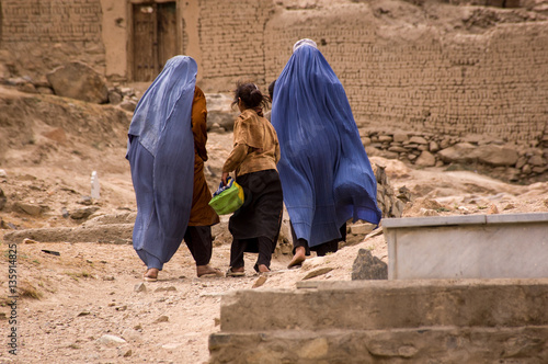 Girls and women in burqas walk through a graveyard near Kabul, Afghanistan photo