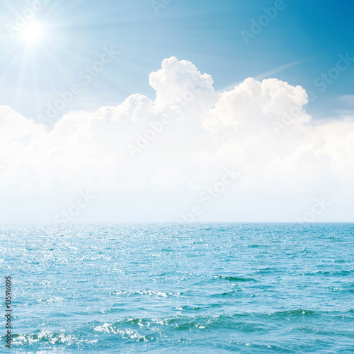 sun in blue sky over white clouds and sea