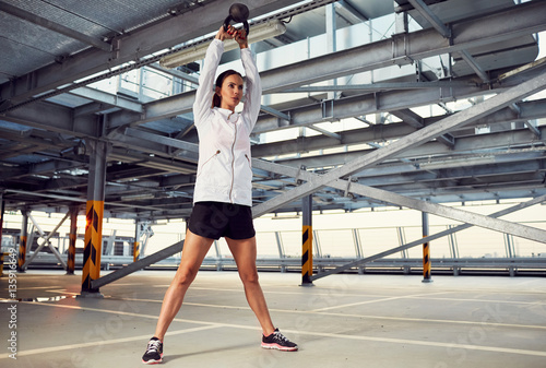 Young woman doing kettlebell swing exercise on parking garage