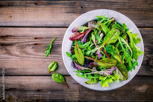 Fresh salad with mixed greens on wooden background