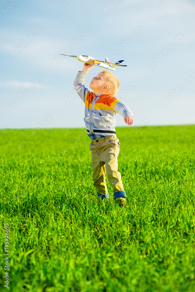 Happy kid playing with toy airplane against blue summer sky background. Boy throw foam plane in green field. Best childhood concept. Happy kid playing with toy airplane against blue summer sky background. Boy throw foam plane in green field. Best childhood concept.