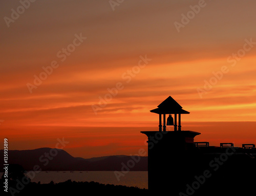 silhouette roof and black giant bell over sea in sunset