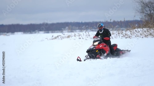 Man driving snowmobile in snowyfield. Snowmobile races. Man on a snowmobile. Winter sports and entertainment. Slow motion. photo