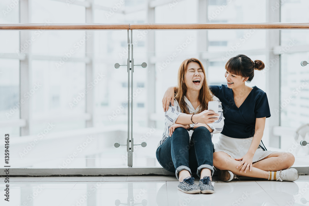Young happy Asian girls best friends laugh and smile while having fun with smart phone mobile indoor. Young happy Asian girls best friends laugh and smile while having fun with smart phone mobile indoor.