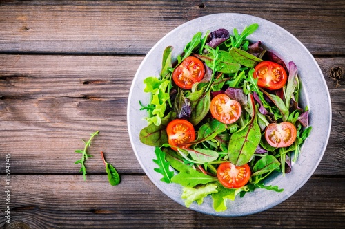 Fresh salad with mixed greens and cherry tomato on wooden background