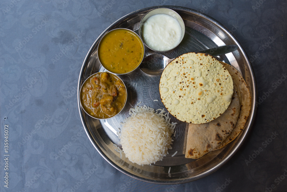 North Indian thali, a tipical meal served on stainless steel plate on blue table. Directly above. North Indian thali, a tipical meal served on stainless steel plate on blue table. Directly above.