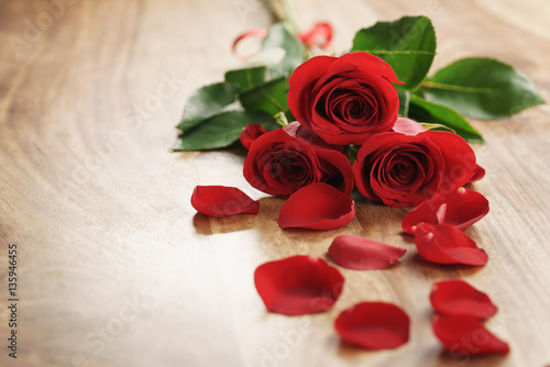 three red roses and petals on old wood table with copy space  romantic background