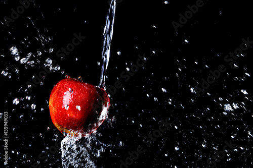 red apple under a waterfall splashing on a black background