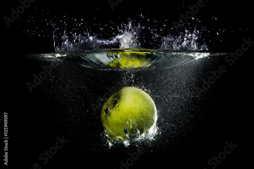 Green apple falling in water with splash on black background. © Sokirlov
