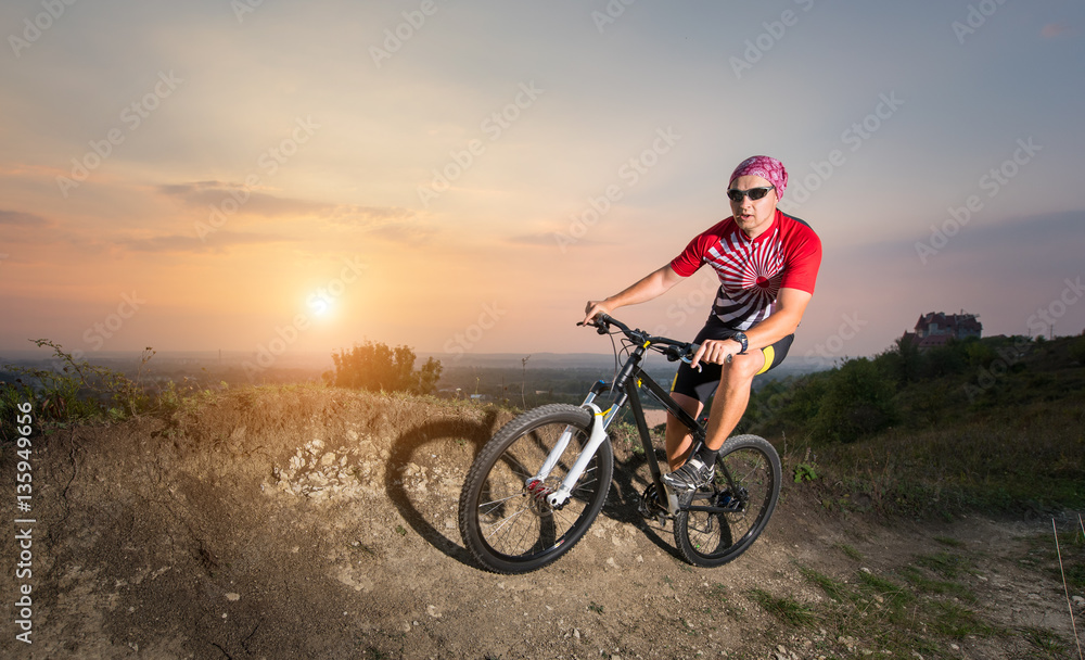 Man in glasses riding on the mountain bicycle on a trail against evening sky with bright sun on the sunset Man in glasses riding on the mountain bicycle on a trail against evening sky with bright sun on the sunset