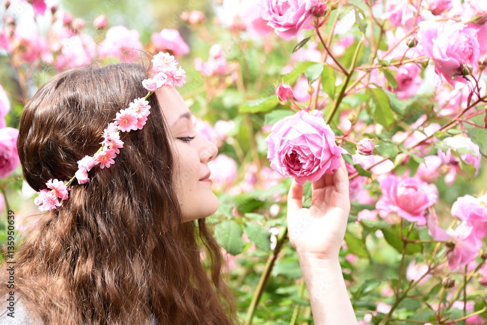 Naklejka premium Girl smells the roses in the garden