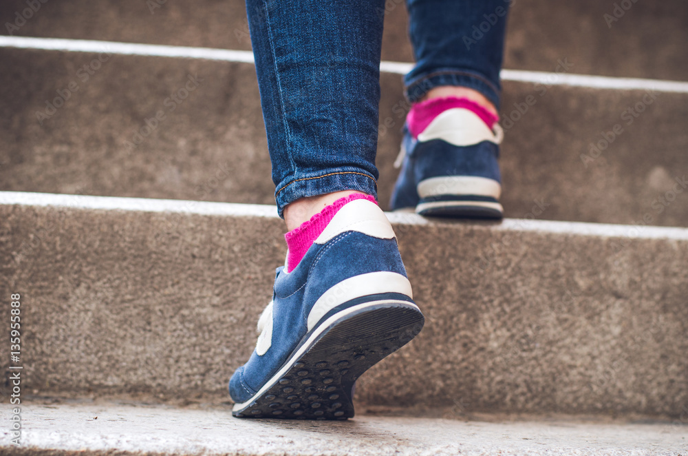 Female feet in denim sneakers on the stairs Female feet in denim sneakers on the stairs
