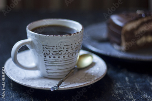 A cup of coffee together with a delicious slice of a chocolate cake on a white and dark worn out background.