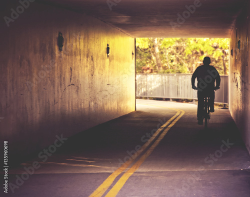  a bicyclist riding through a dark tunnel during summer