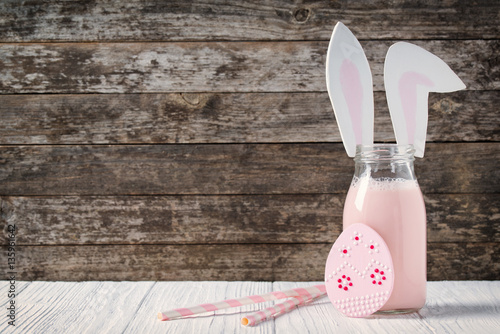Easter cookie and bottle of strawberry milk with cute rabbit ears on wooden background