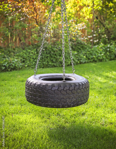 an old rubber tire swing on chains in a backyard for kids to pla photo