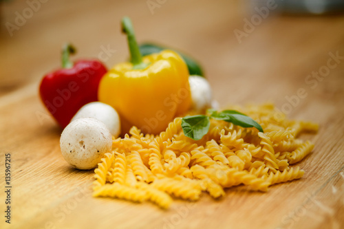 fresh vegetables and pasta lying on a wooden table.