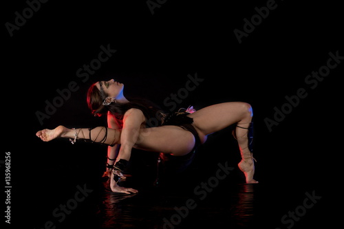 Obraz na plátně woman athlete gymnast in the form of an elf performs acrobatics on a black background in the scenic red and blue light