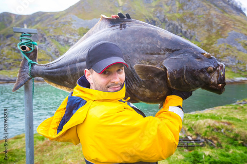 Bild auf Leinwand fisherman carries on his shoulder a huge fish. 25 kg halibut.