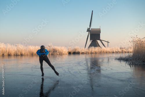Ice skating past frosted reeds and a windmill