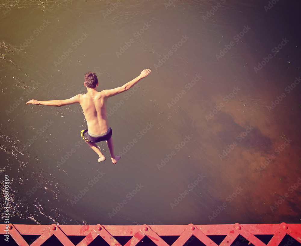 a boy jumping of an old train trestle bridge into a river done with a retro instagram filter