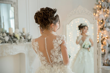 Beautiful bride in a wedding dress at a mirror in Christmas. 