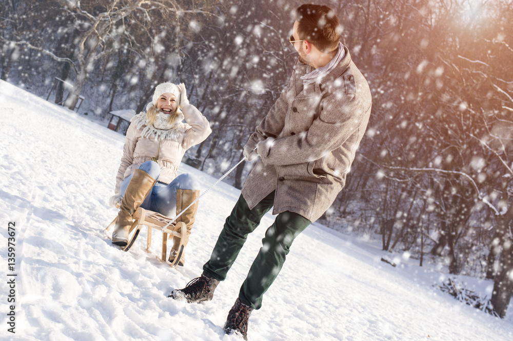 Fototapeta premium Young Couple Sledding And Enjoying While Snow Falling