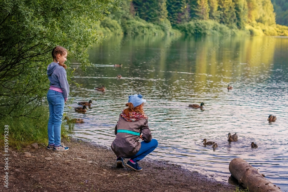 Children girls in the lake in the mountains to feed the ducks. Children girls in the lake in the mountains to feed the ducks.